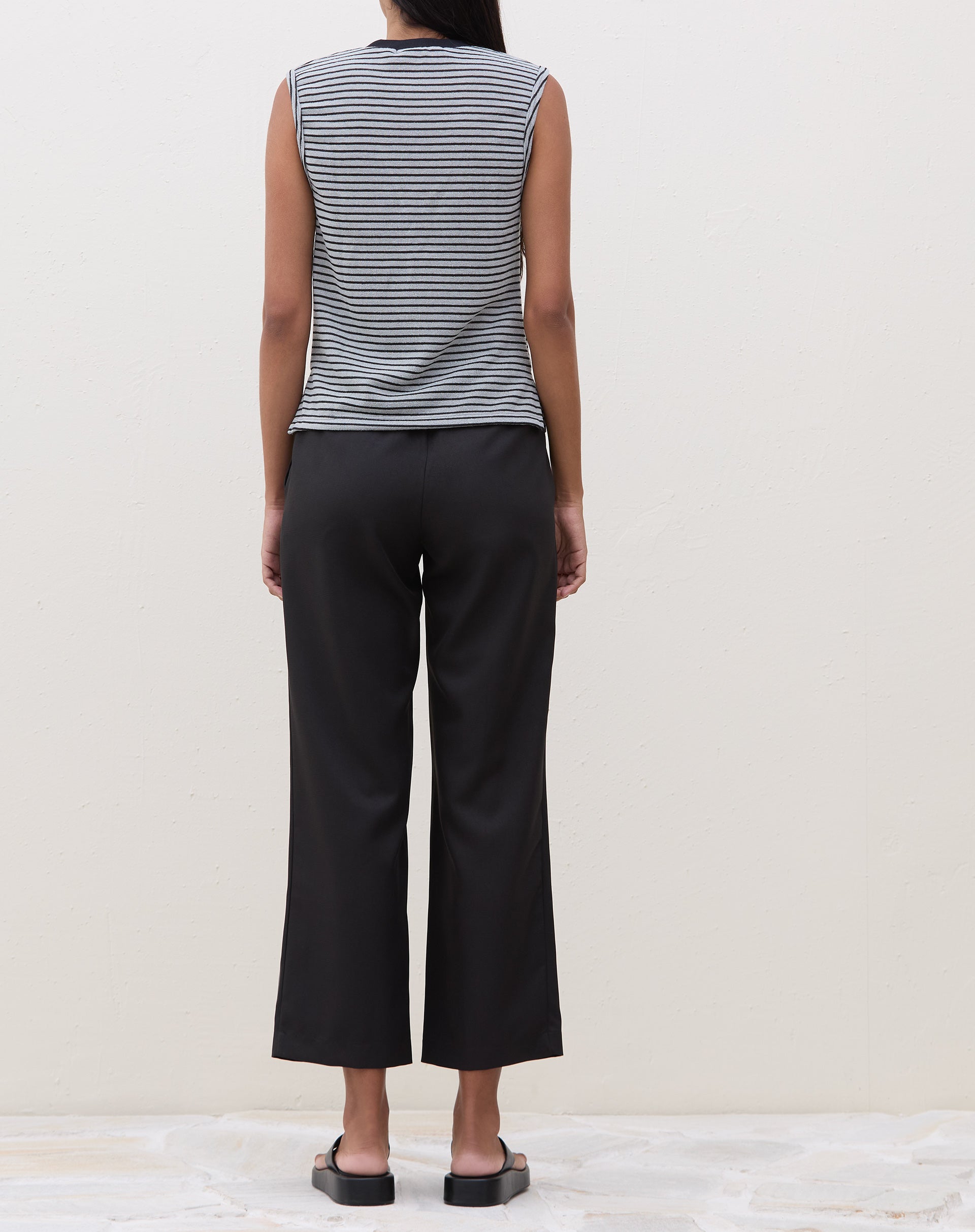 Modelo vestindo calça reta preta com cós transpassado, vista traseira.