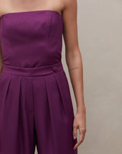 Detalhe do cós transpassado da calça reta roxa, destacando o botão decorativo.