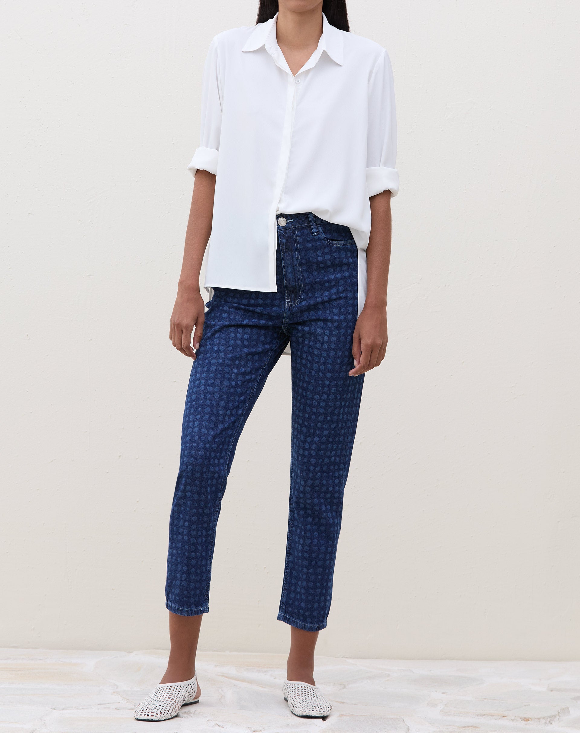 Modelo vestindo calça Mom Jeans azul médio com estampa de bolinhas, combinada com camisa branca.