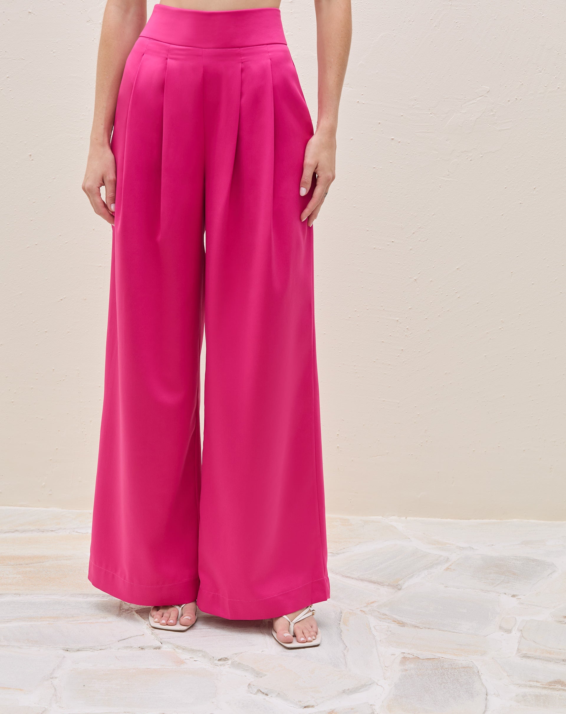 Modelo vestindo calça wide leg rosa escuro com pregas e top branco, vista lateral.