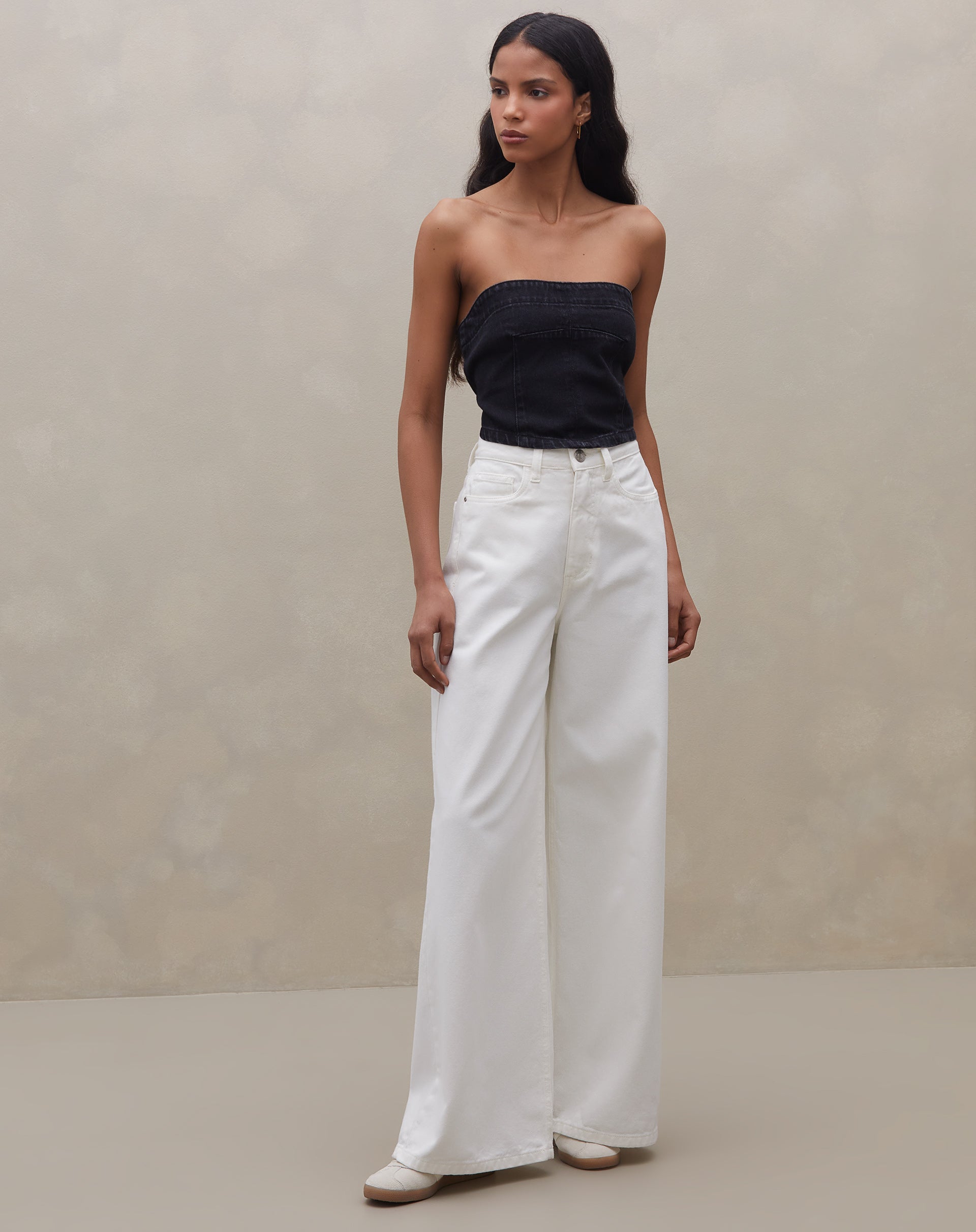 Modelo vestindo o top sem alça jeans preto combinado com calça branca ampla.