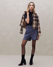 Modelo vestindo shorts azul com vivo contrastante, combinado com blusa preta e jaqueta xadrez.