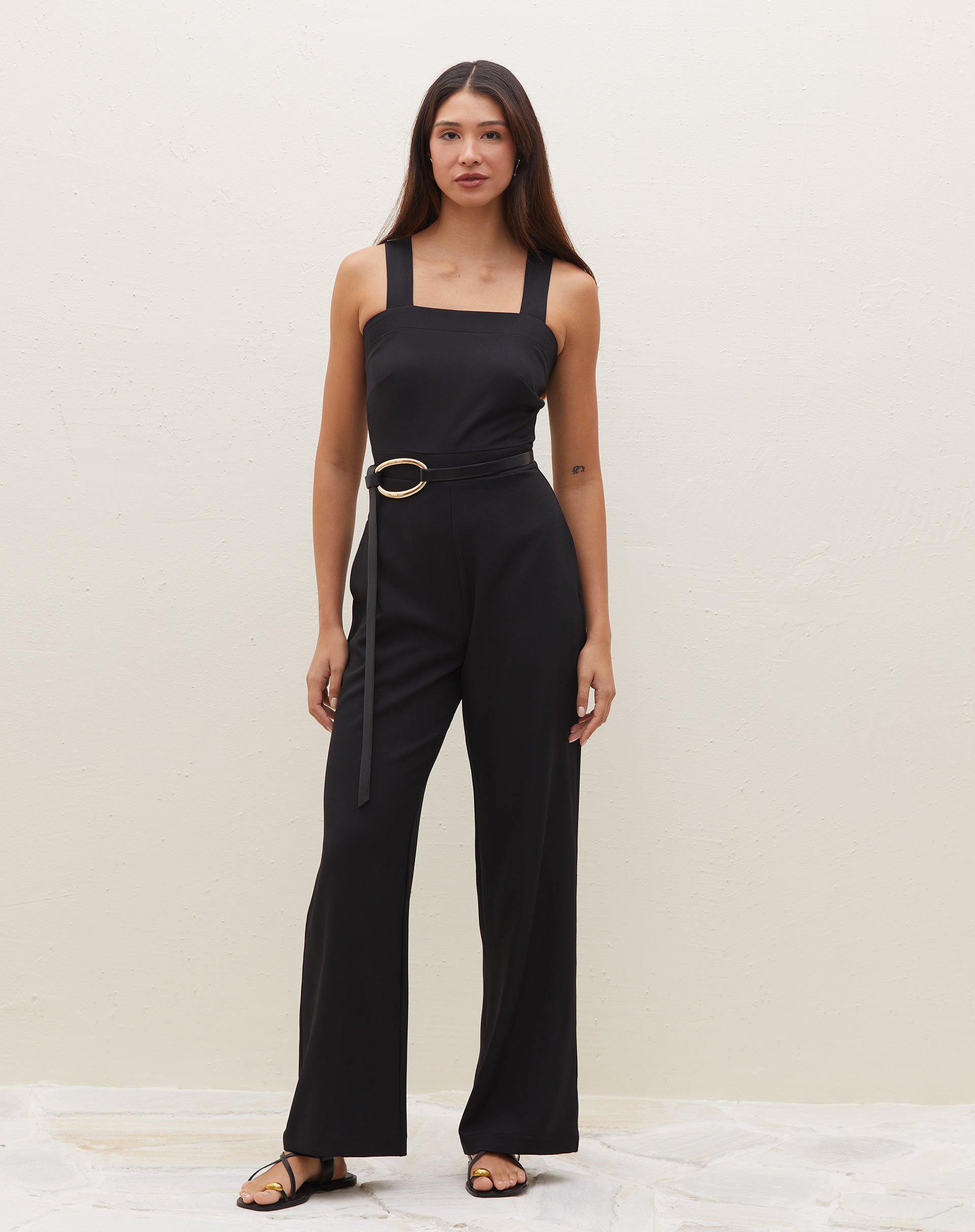 Imagem de frente do macacão preto com alças largas, mostrando seu design elegante.