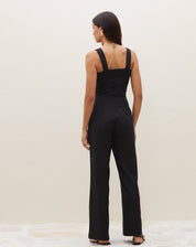 Vista traseira do macacão preto, destacando o decote reto nas costas e alças largas.