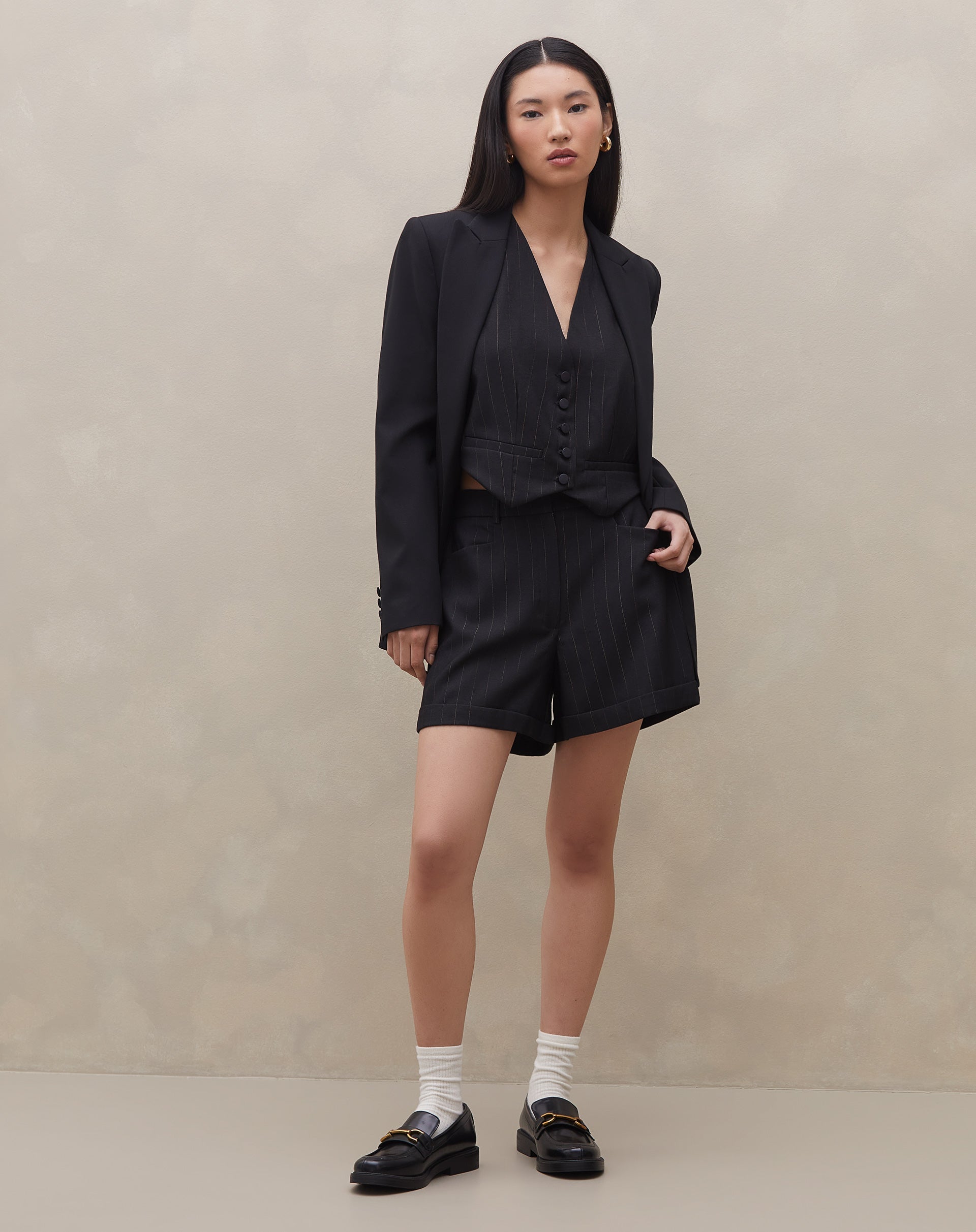 Modelo usando shorts evasê preto com risca de giz e blazer preto.