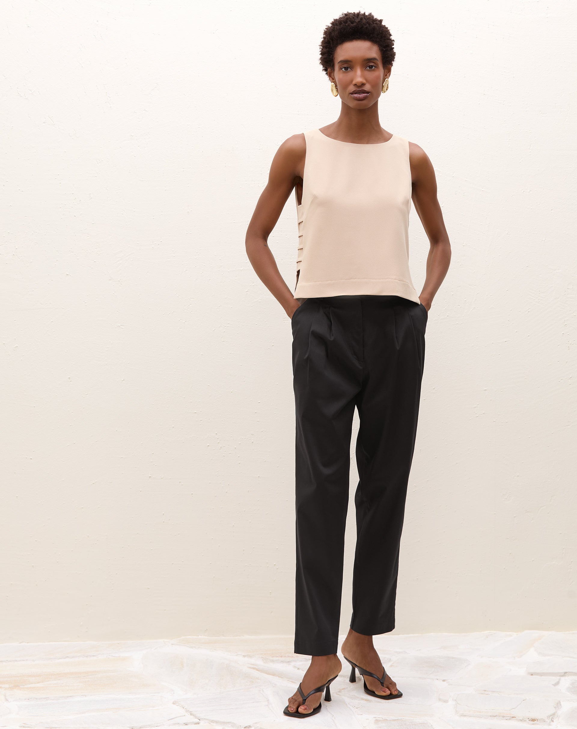 Modelo vestindo calça de alfaiataria baggy preta com pregas e blusa bege, vista frontal.