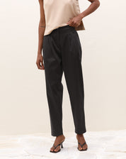 Modelo vestindo calça de alfaiataria baggy preta com pregas e blusa bege, vista lateral.