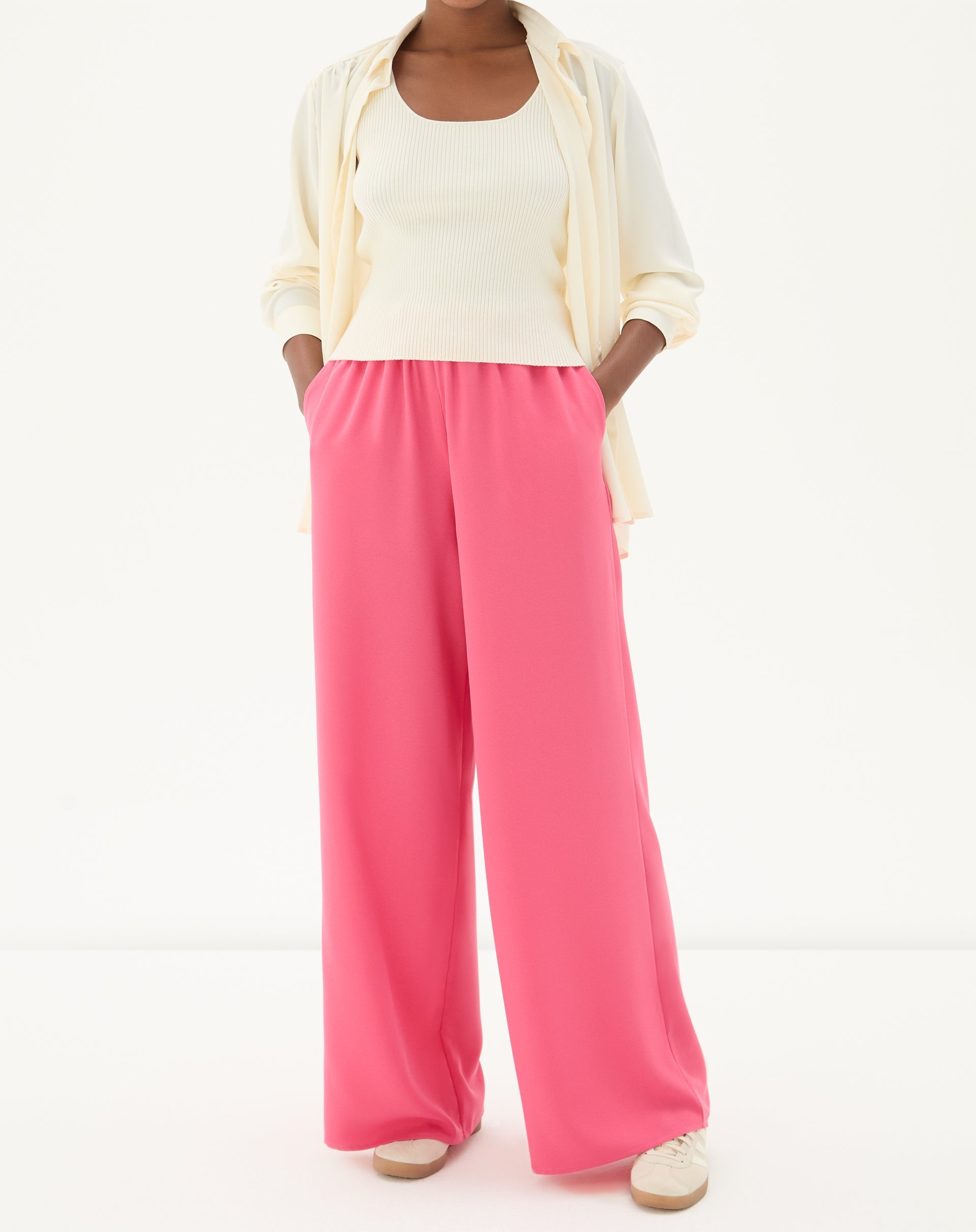 Modelo vestindo calça wide leg coral com cós elástico e pregas, combinada com camisa leve.