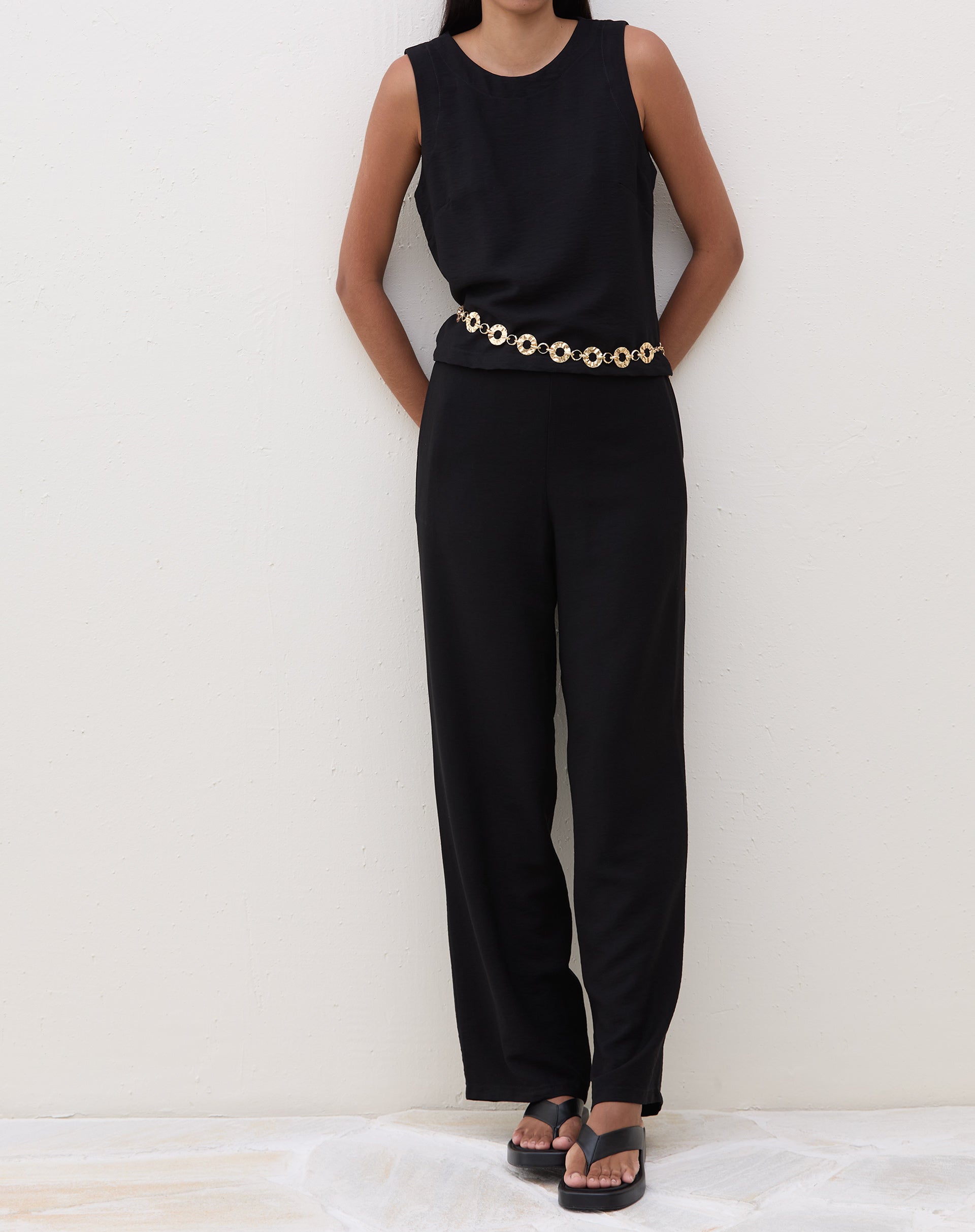 Modelo vestindo calça preta reta com cós elástico, combinada com blusa preta e sandália.