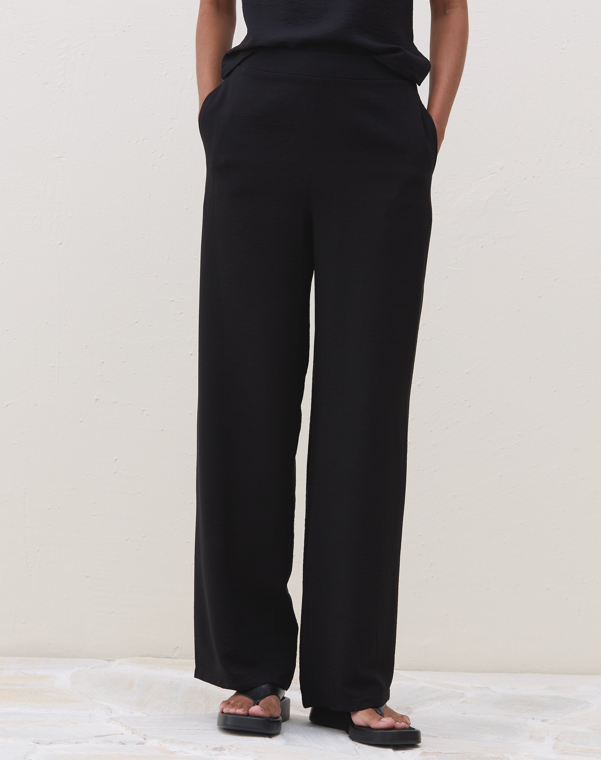 Detalhe do cós elástico da calça preta reta.