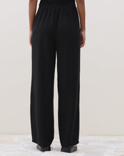 Modelo vestindo calça preta reta com cós elástico, combinada com blusa preta e sandália.