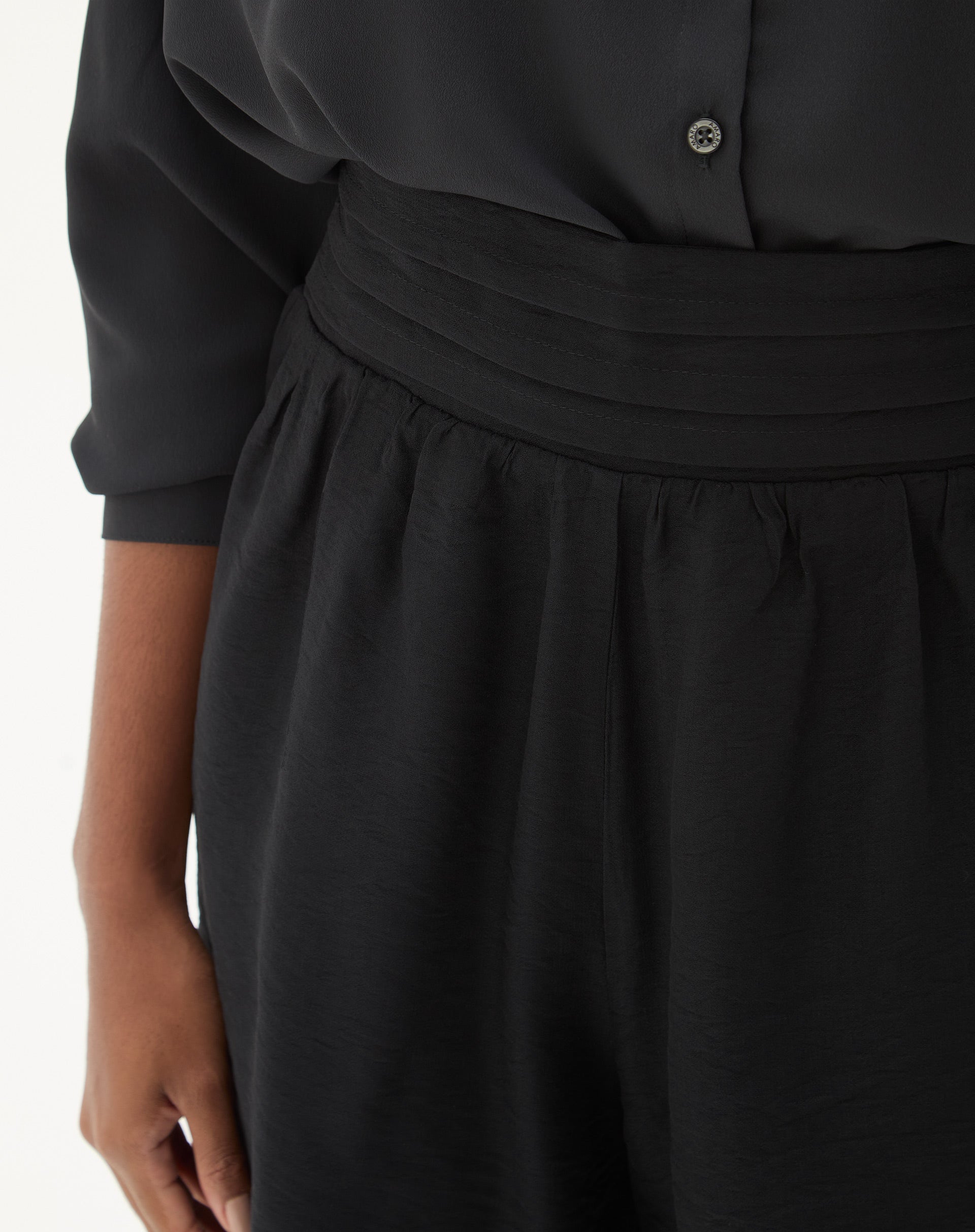 Modelo vestindo shorts preto com sandálias pretas e camiseta branca.