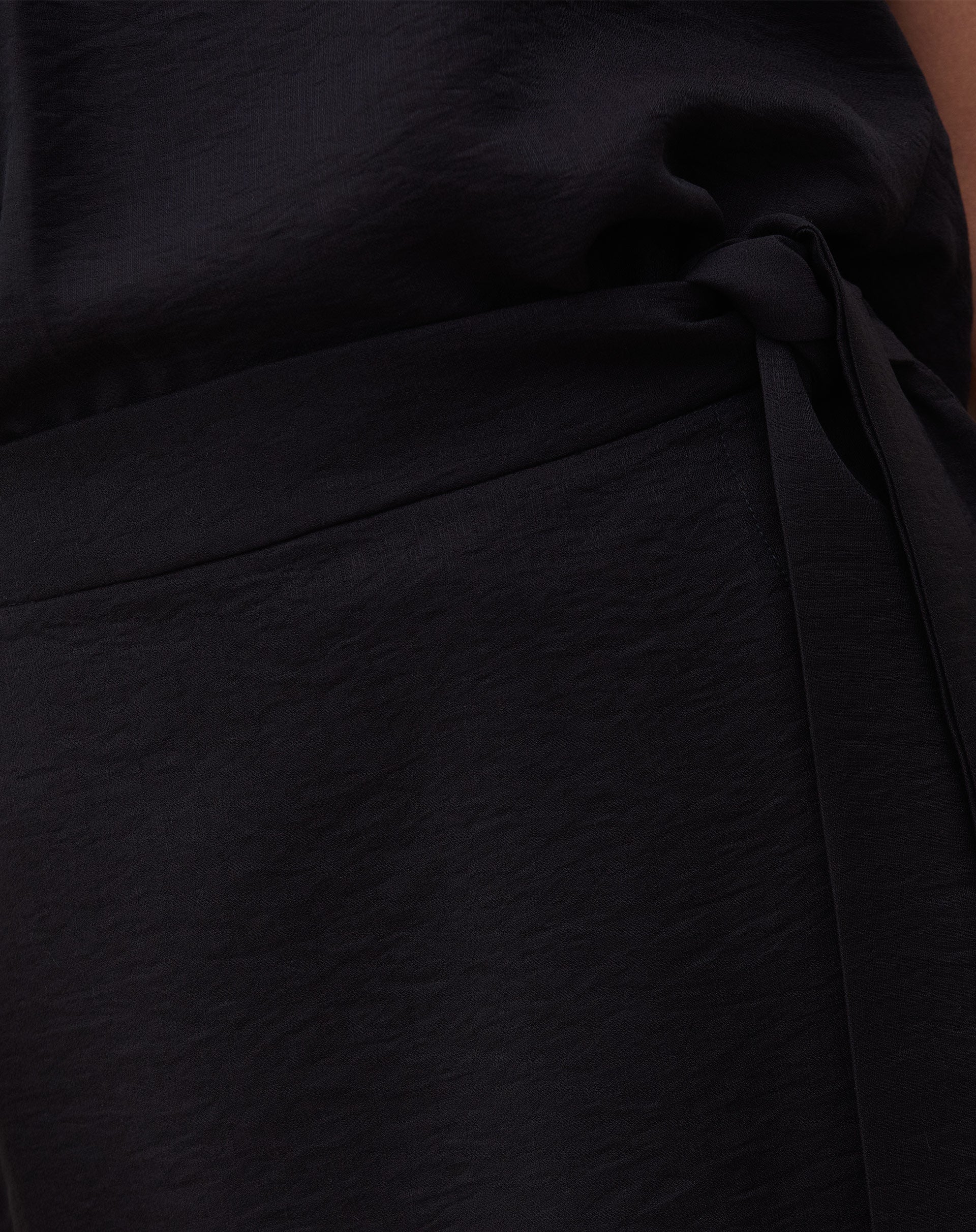 Vista lateral da saia curta transpassada preta.