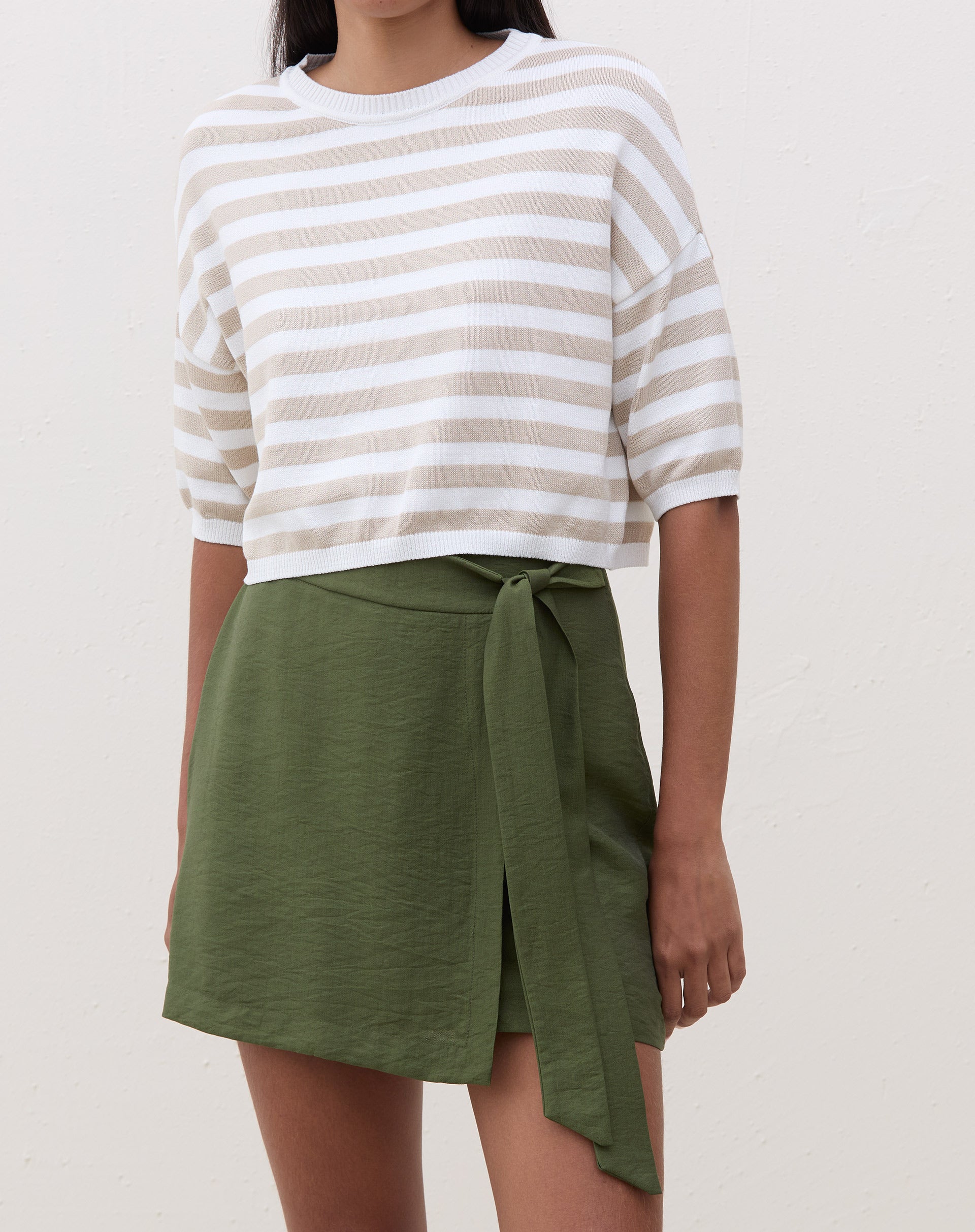 Modelo vestindo saia curta transpassada verde militar com blusa listrada.