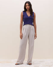 Modelo vestindo calça cinza claro com cintura alta e pregas, combinada com top azul sem mangas.