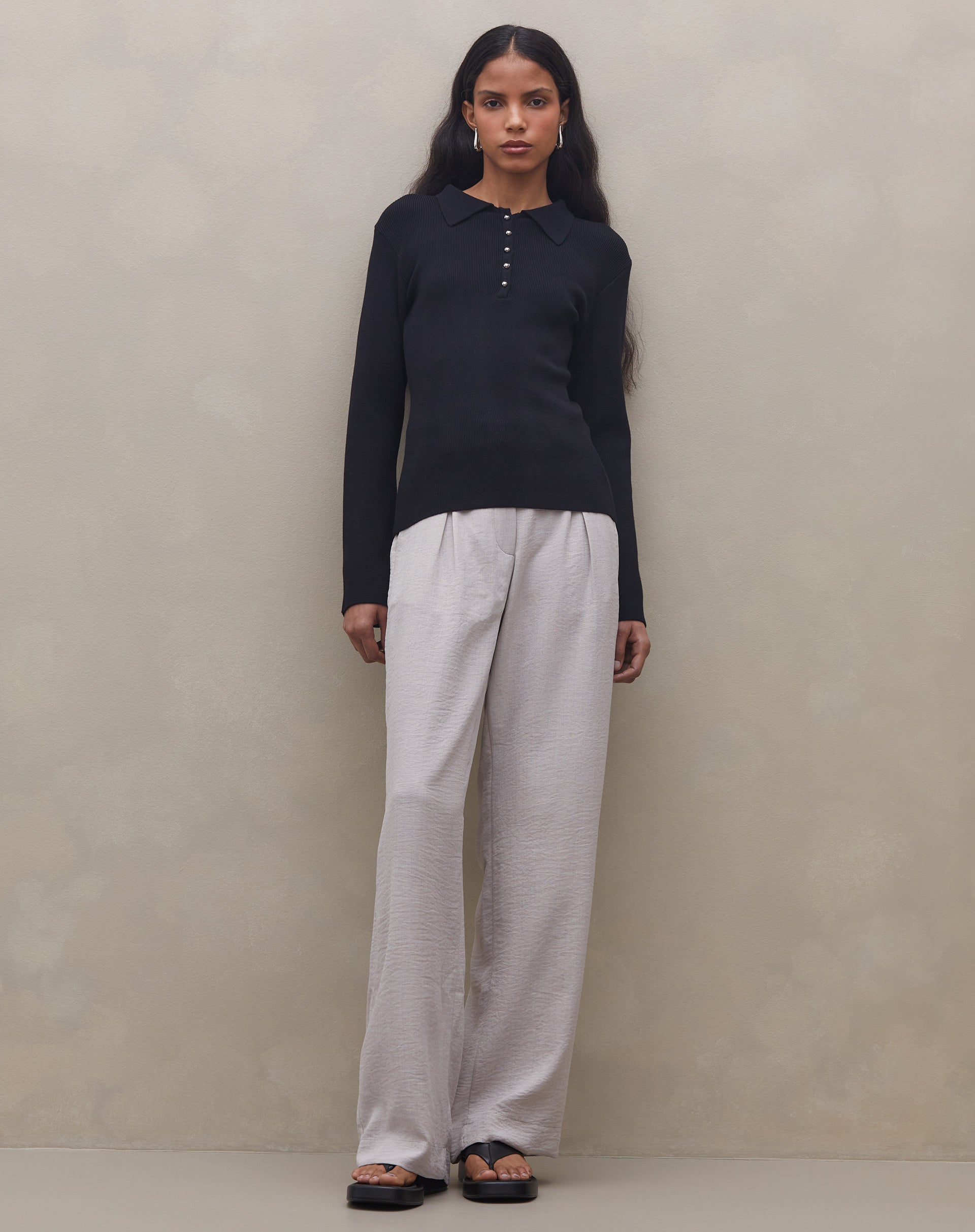 Modelo vestindo calça cinza claro com cintura alta, combinada com blusa preta de mangas longas.