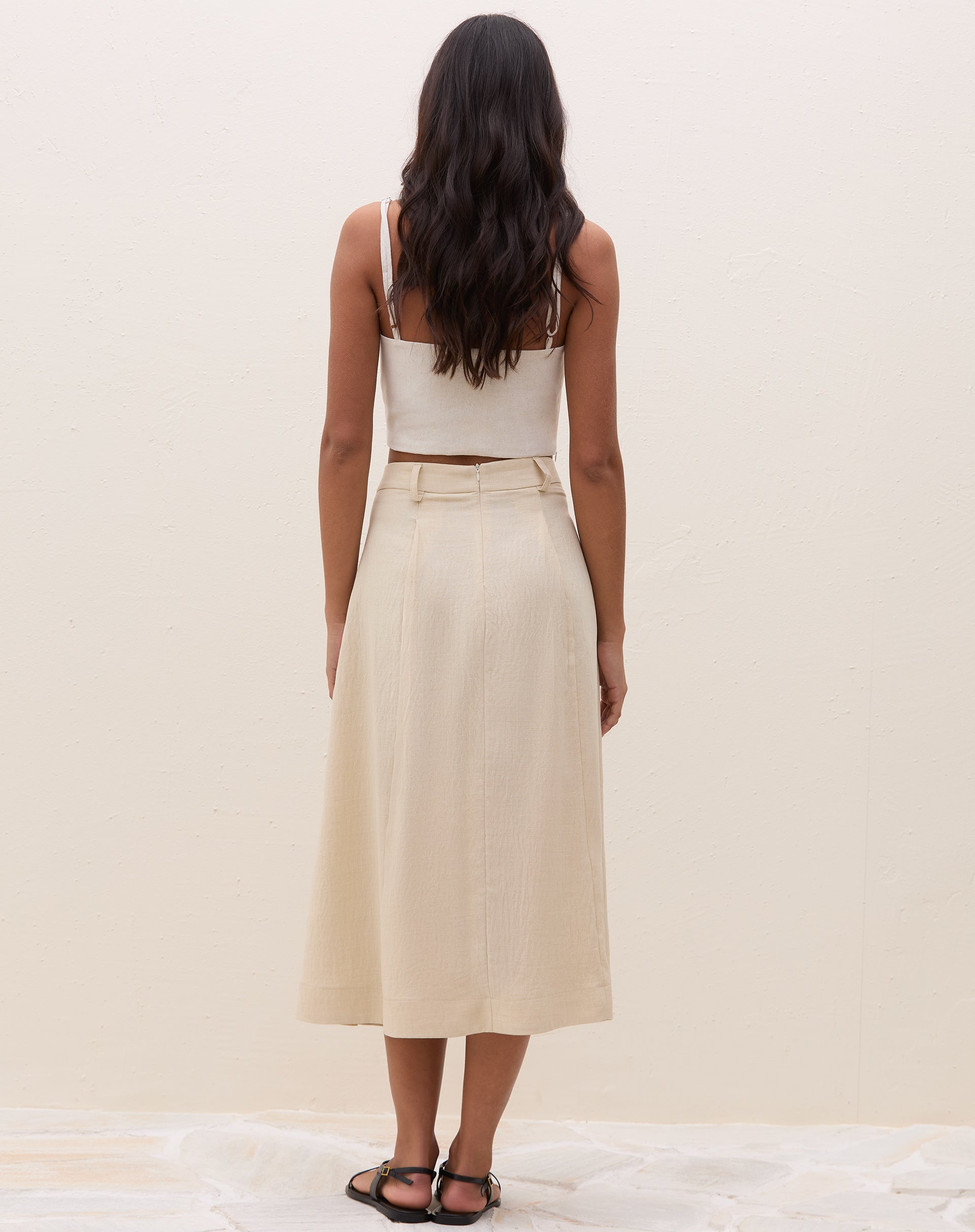 Modelo vestindo saia midi off-white com pregas, vista lateral.