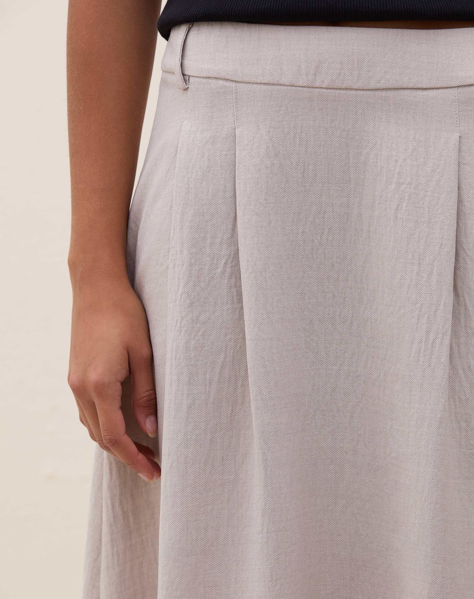 Detalhe da cintura alta e pregas da saia midi cinza claro.