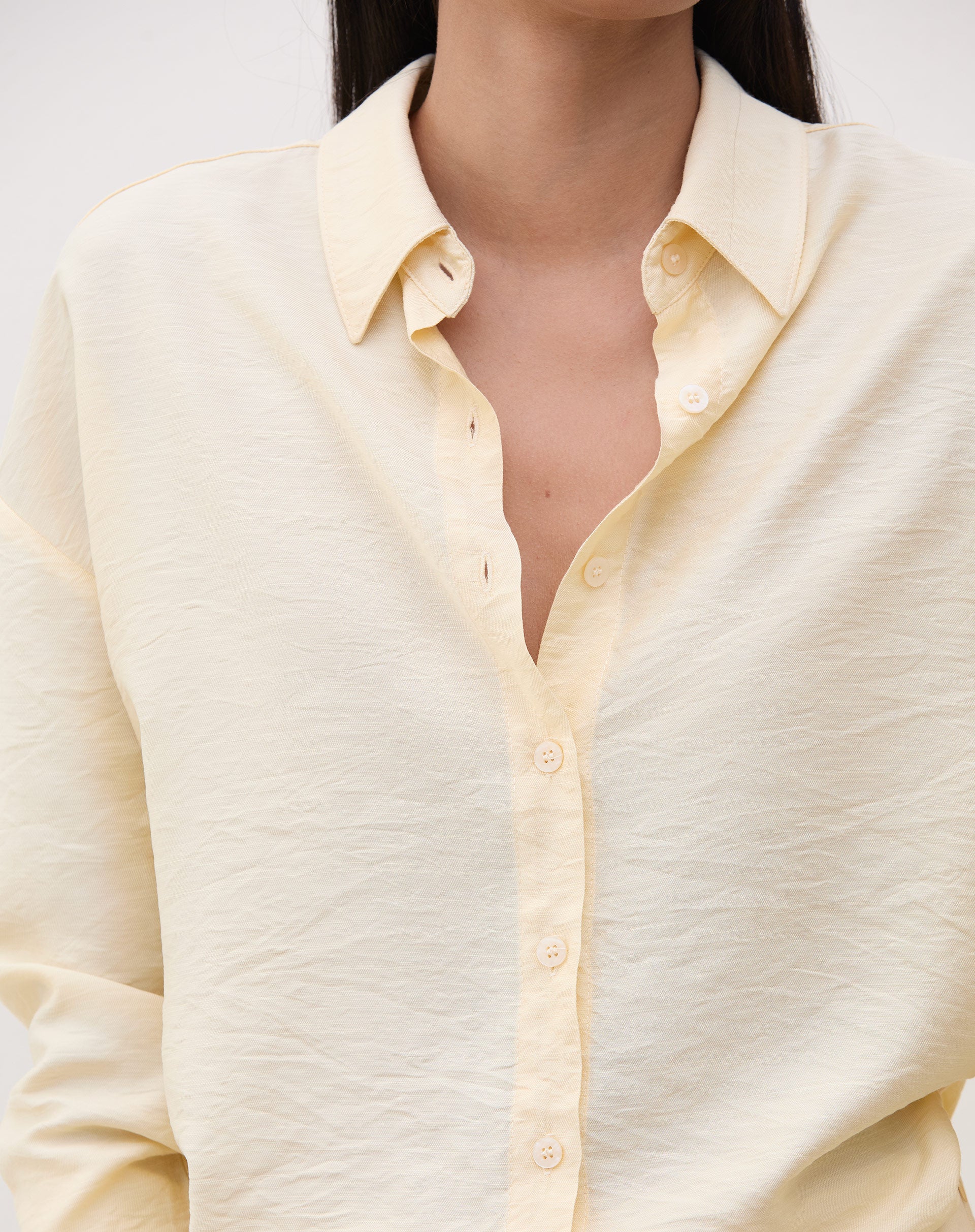 Camisa manga longa em tecido manteiga, vista de perto mostrando detalhes do colarinho e botões.