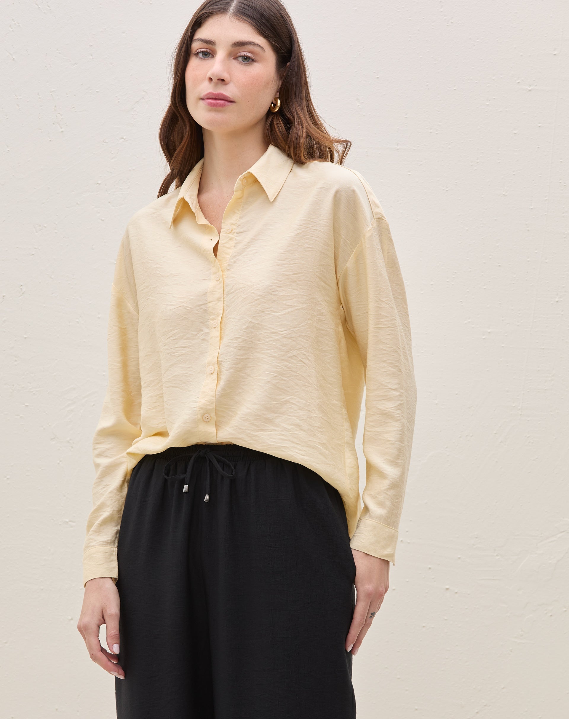 Modelo vestindo camisa manga longa em tecido manteiga, combinada com calça preta.