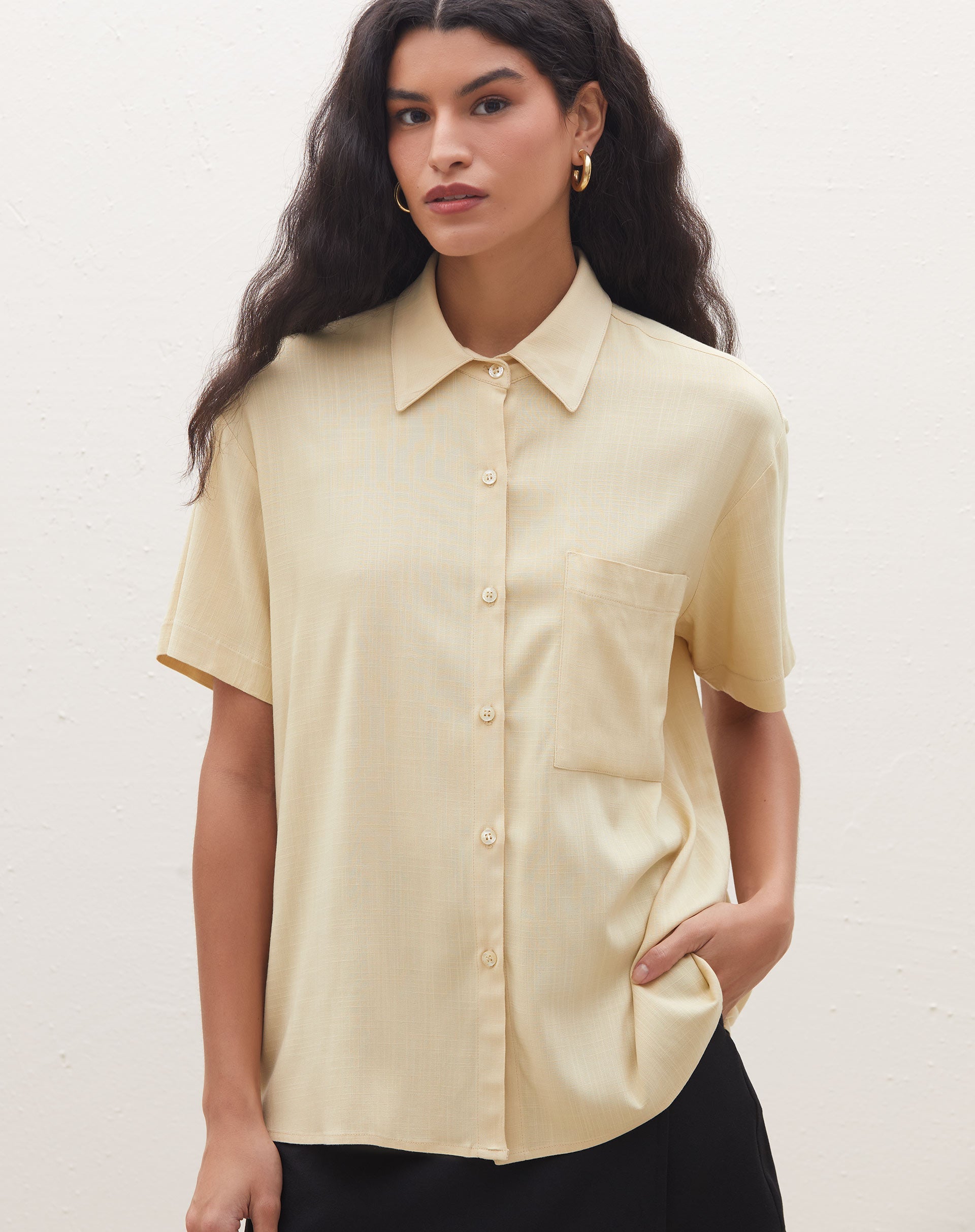 Detalhe da camisa manga curta com bolso em tom areia, mostrando o colarinho e fechamento com botões.