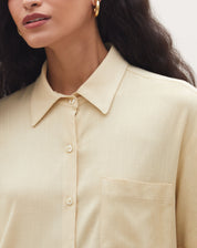 Modelo usando camisa manga curta com bolso em tom areia, vista lateral.