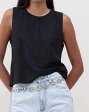 Modelo vestindo regata preta com alças largas e recorte frontal, combinada com jeans claro.