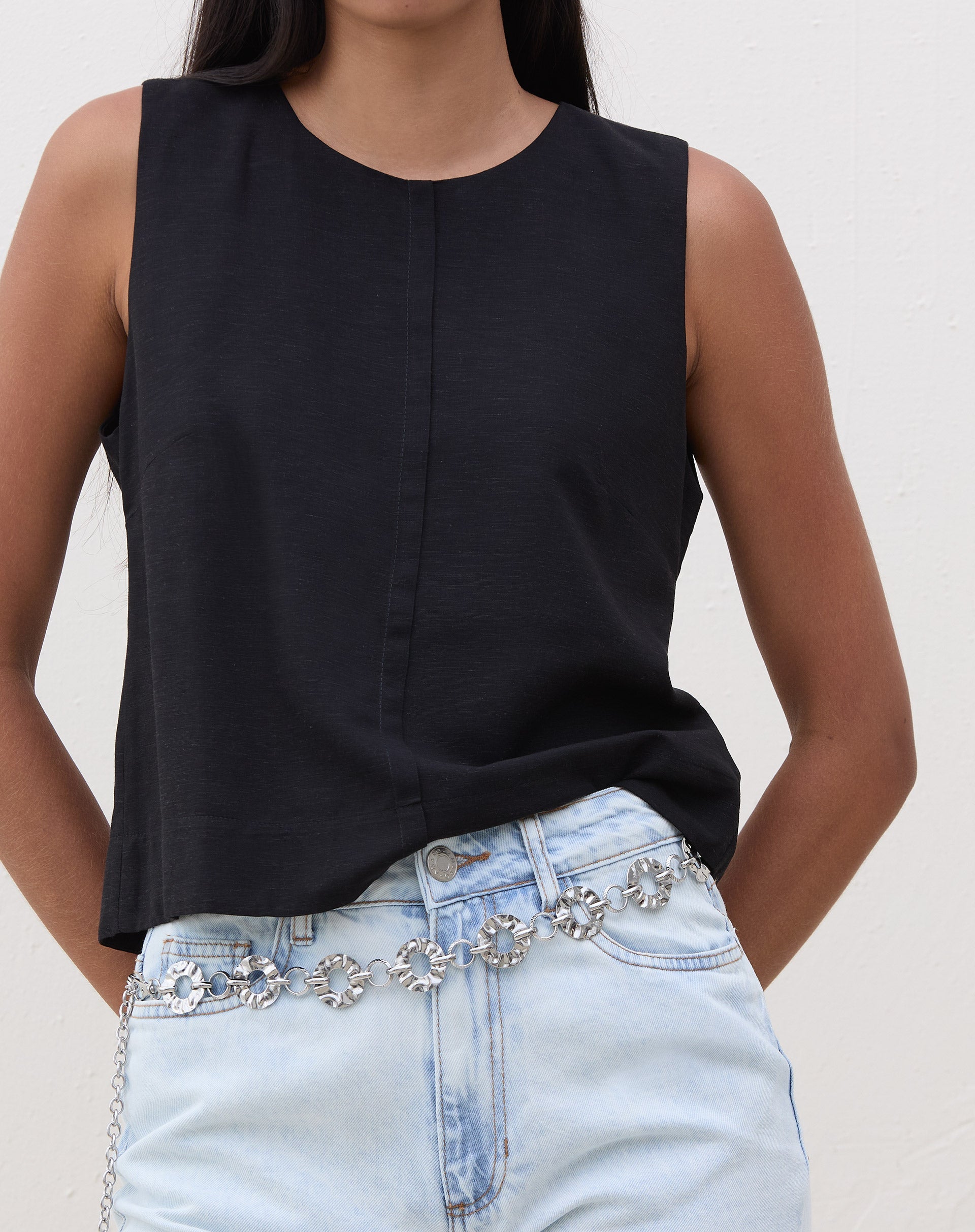 Modelo vestindo regata preta com alças largas e recorte frontal, combinada com jeans claro.