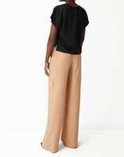 Modelo vestindo blusa preta com calça bege, vista traseira.