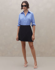 Modelo vestindo saia curta transpassada preta com camisa azul, vista frontal.