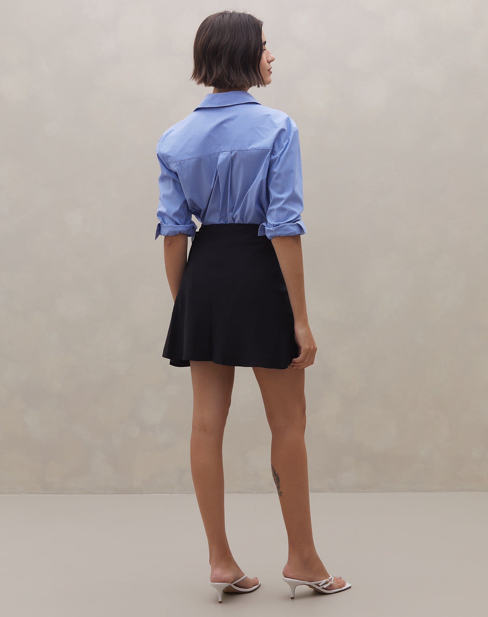 Vista traseira da saia curta transpassada preta com camisa azul.