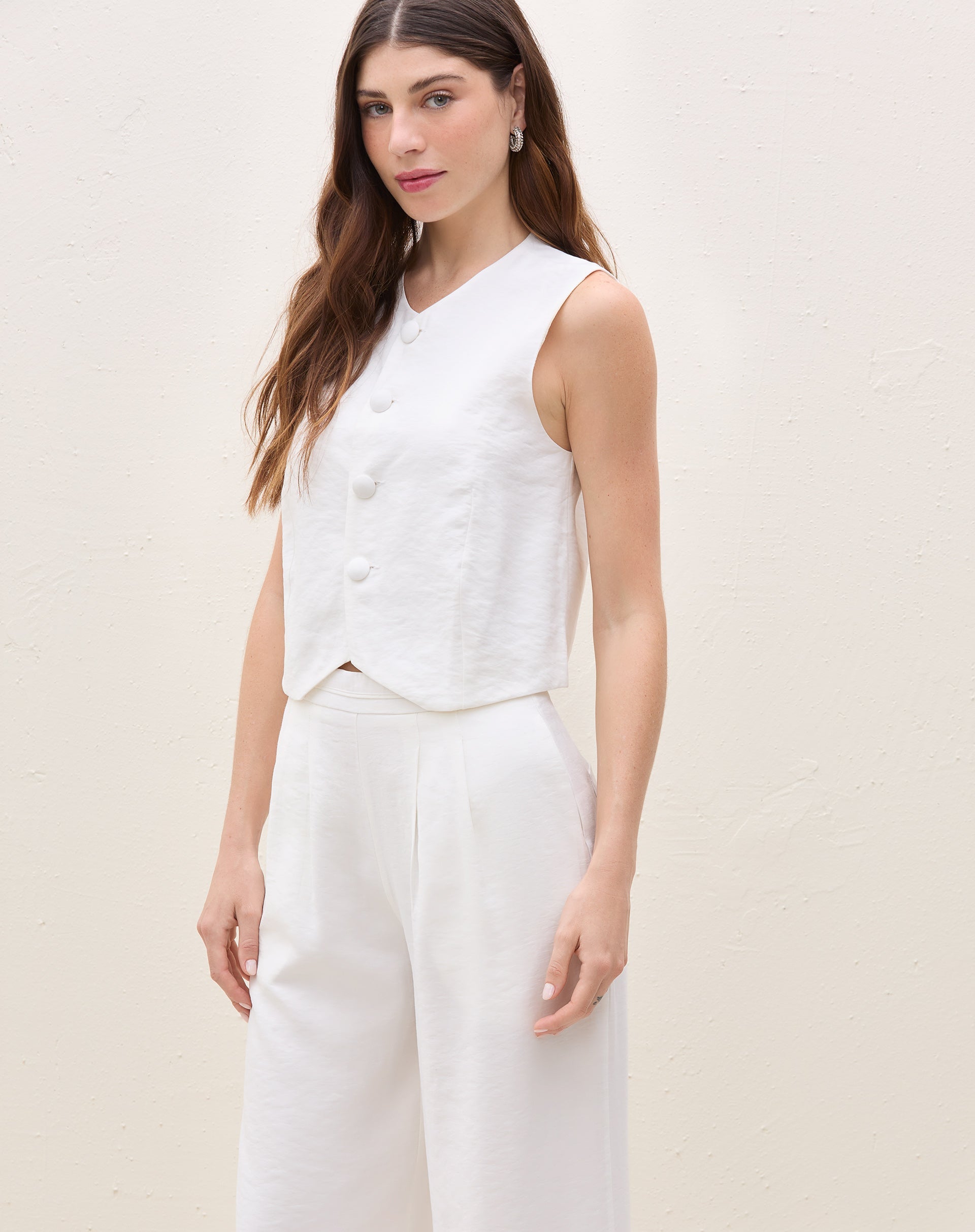 Modelo vestindo calça wide leg off-white com pregas, vista lateral.