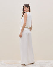 Modelo vestindo calça wide leg off-white com pregas, vista traseira.