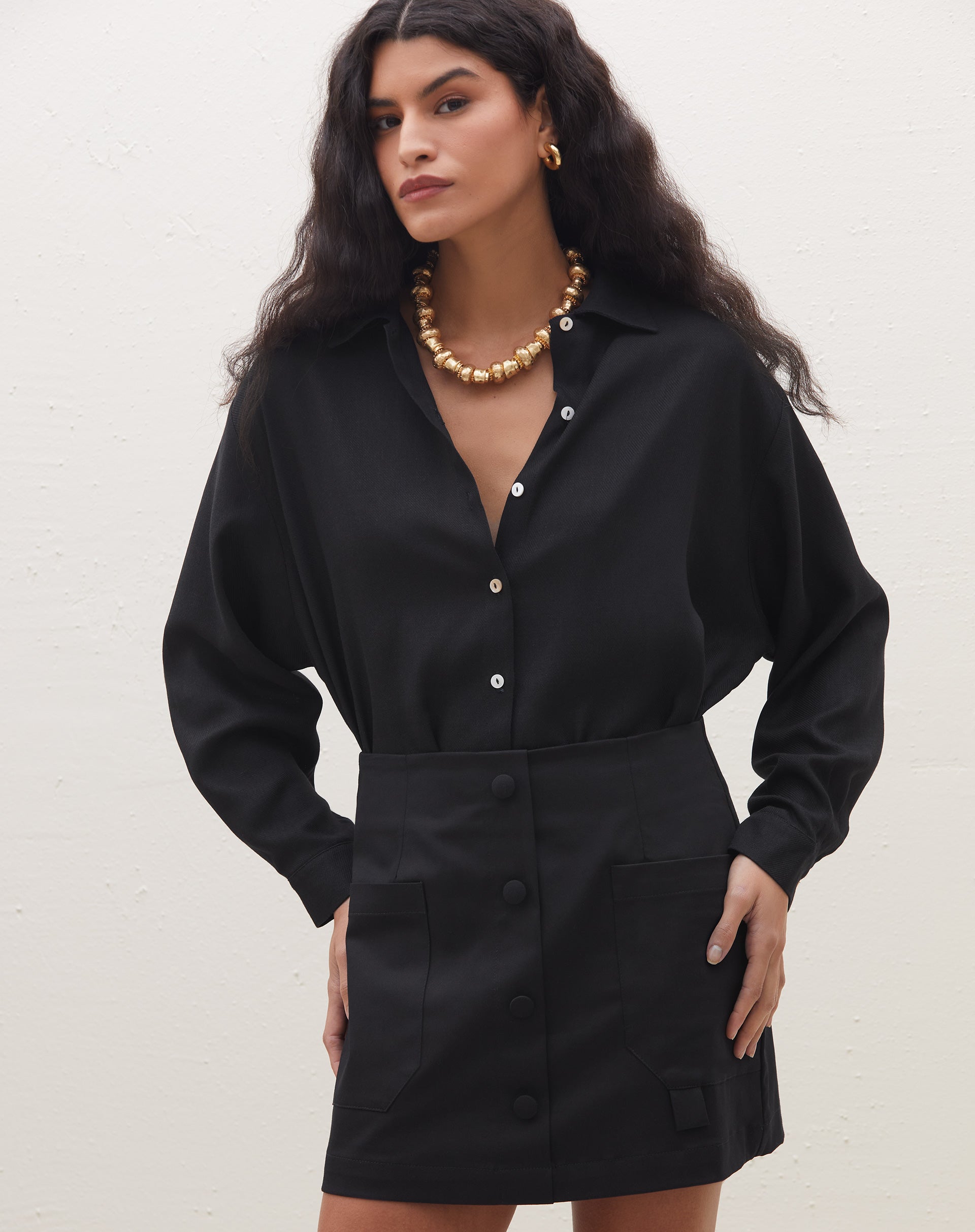 Modelo vestindo saia preta com vista de botões em alfaiataria, combinada com camisa preta.