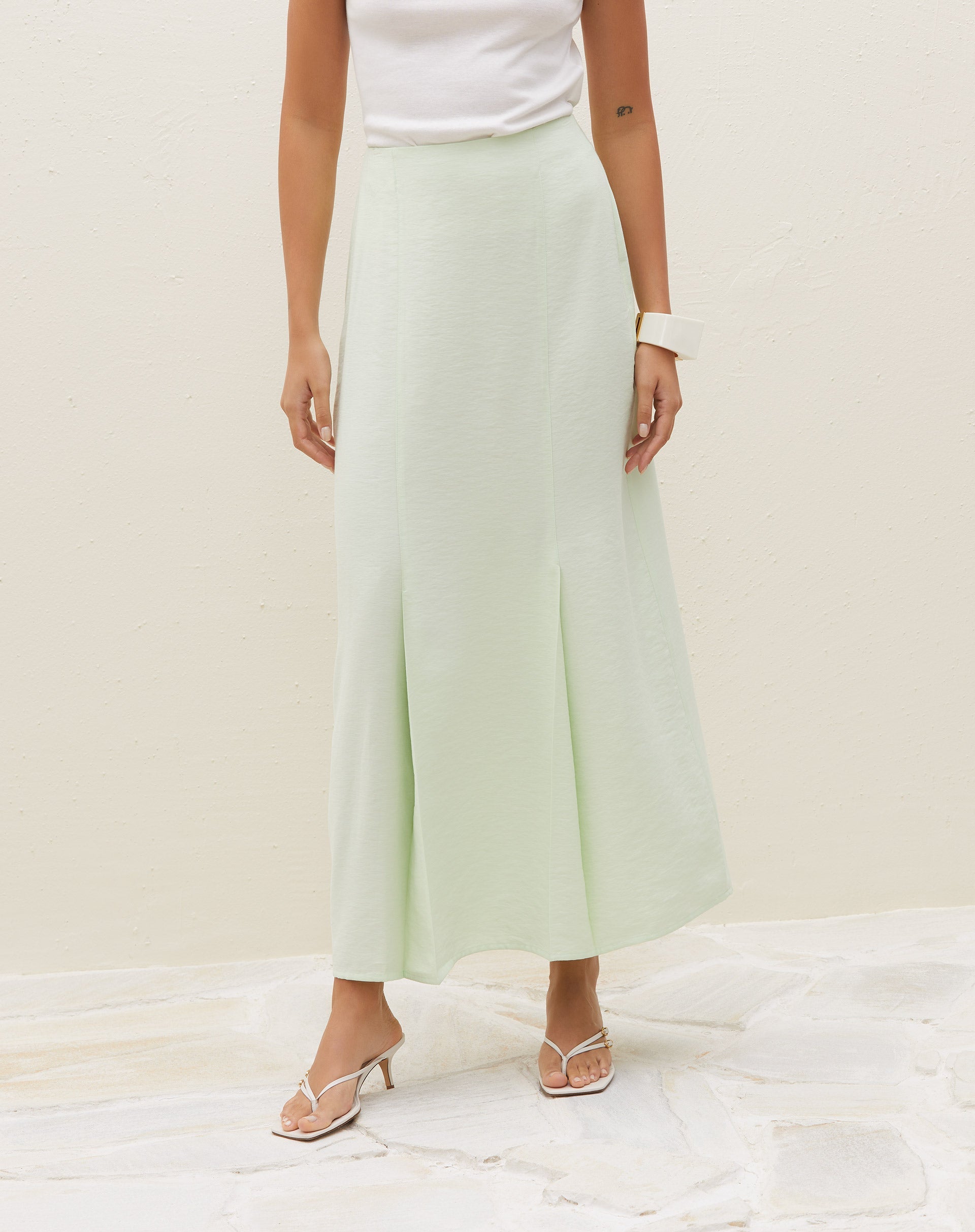 Modelo vestindo saia midi verde claro com pregas, vista lateral.