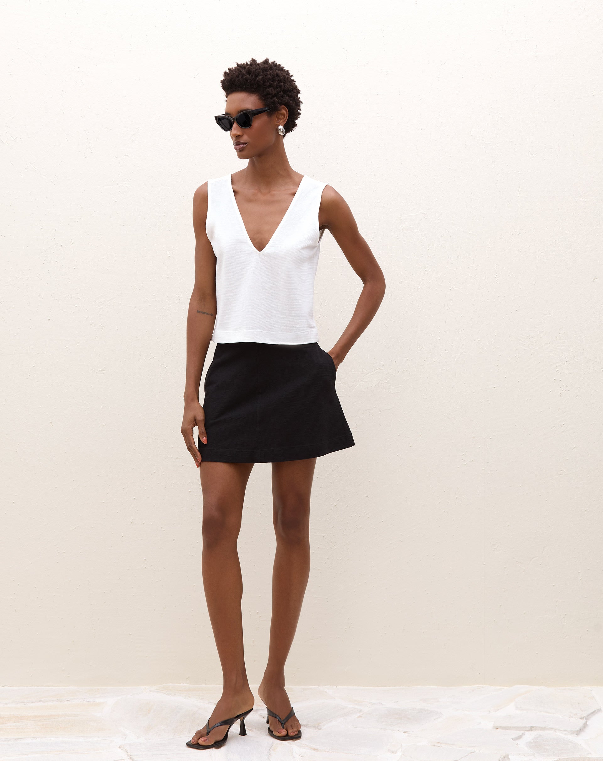 Modelo vestindo saia evasê de malha preta com blusa branca vista de frente.