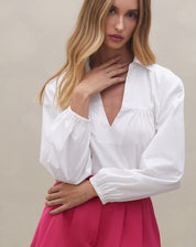 Detalhe da camisa branca com decote em V, complementando o shorts rosa.