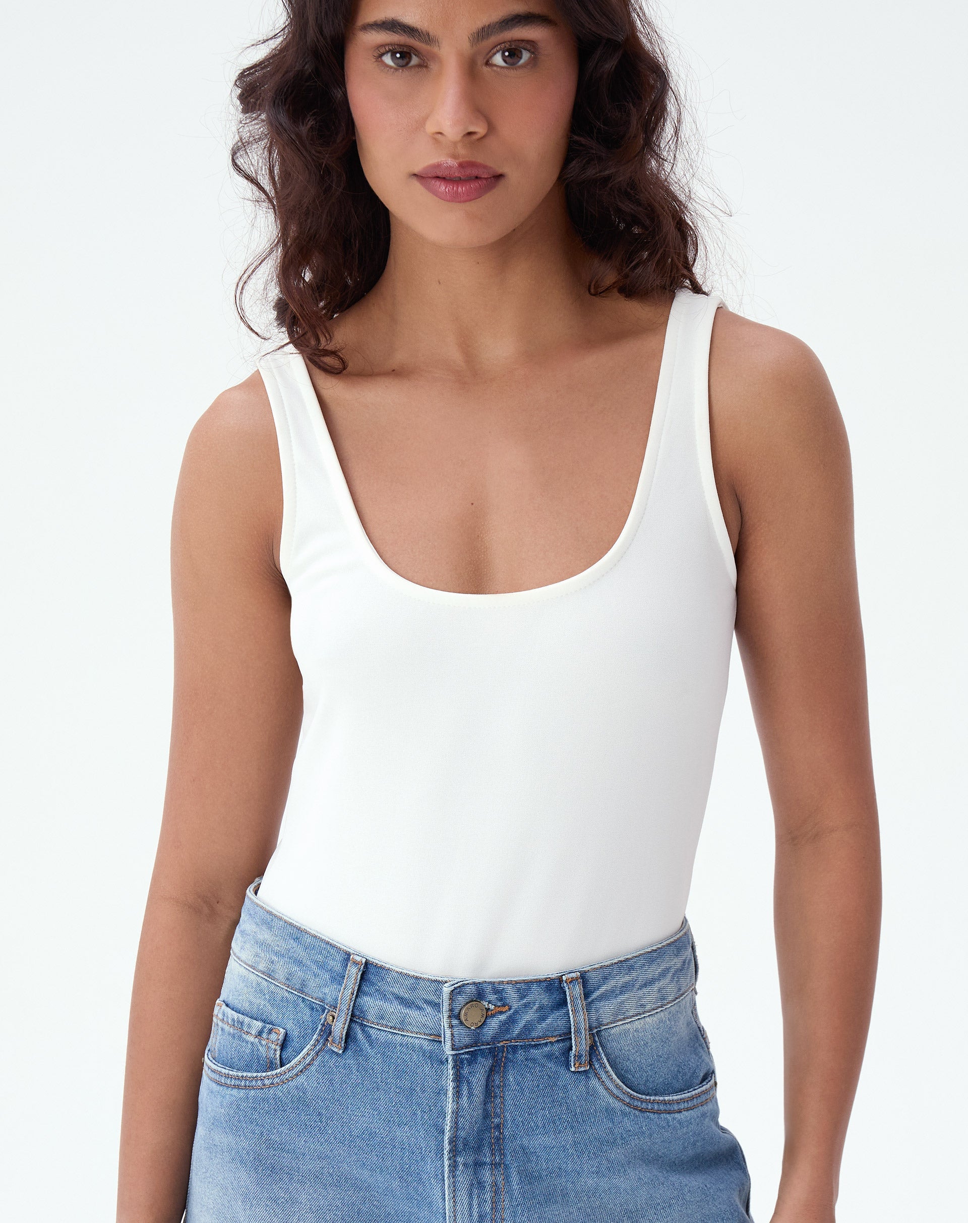 Modelo vestindo body regata de malha creponada em off-white, combinado com jeans.