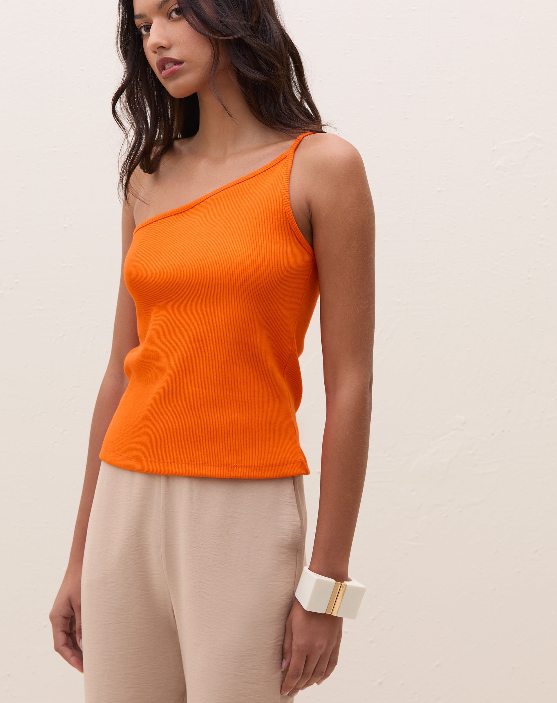 Modelo vestindo blusa um ombro só de ribana power laranja com calça bege.