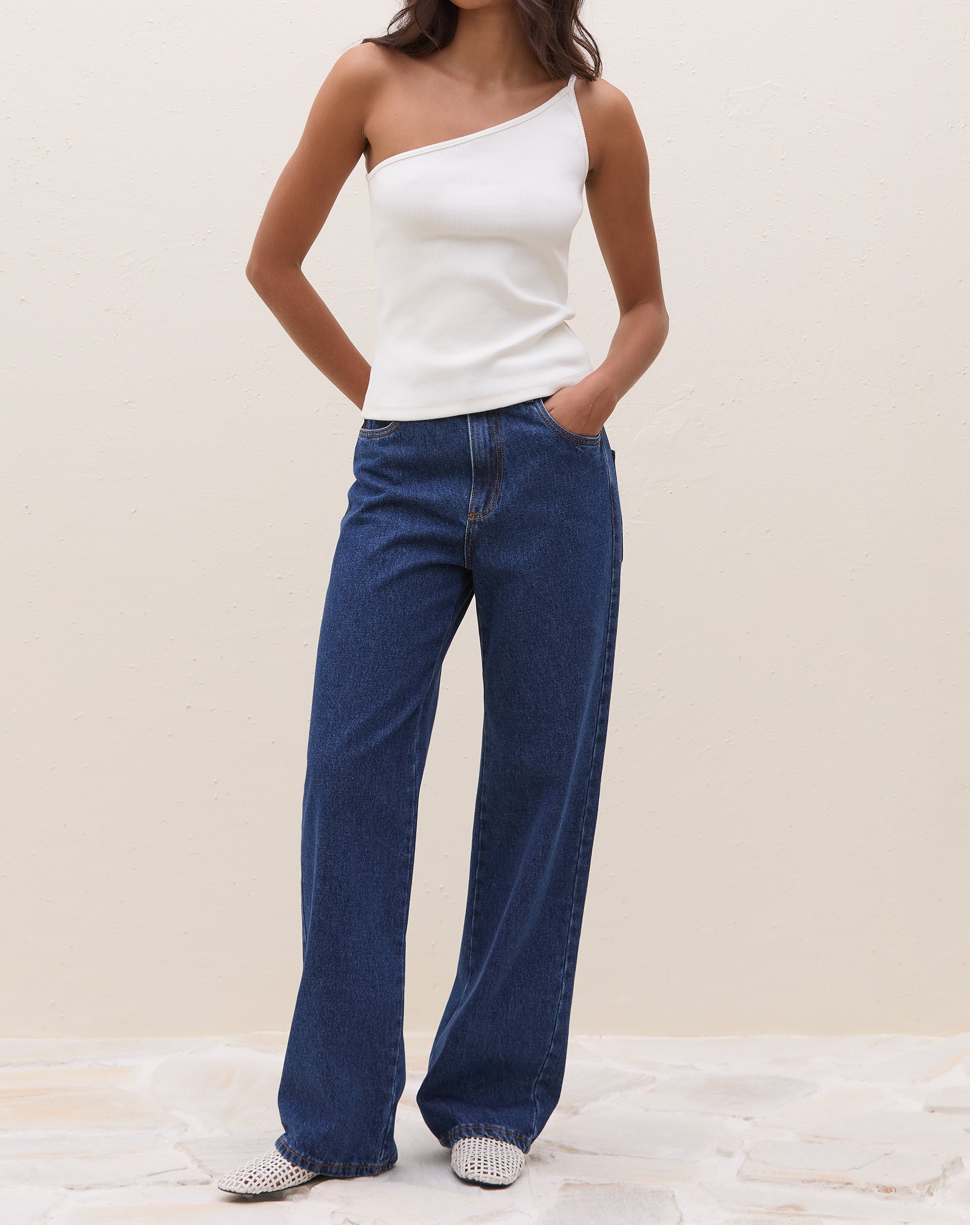 Modelo vestindo a blusa um ombro só de ribana power off-white com calça jeans.