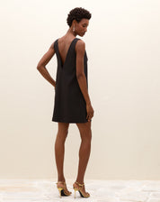 Modelo vestindo um vestido curto preto com decote V nas costas, vista lateral.