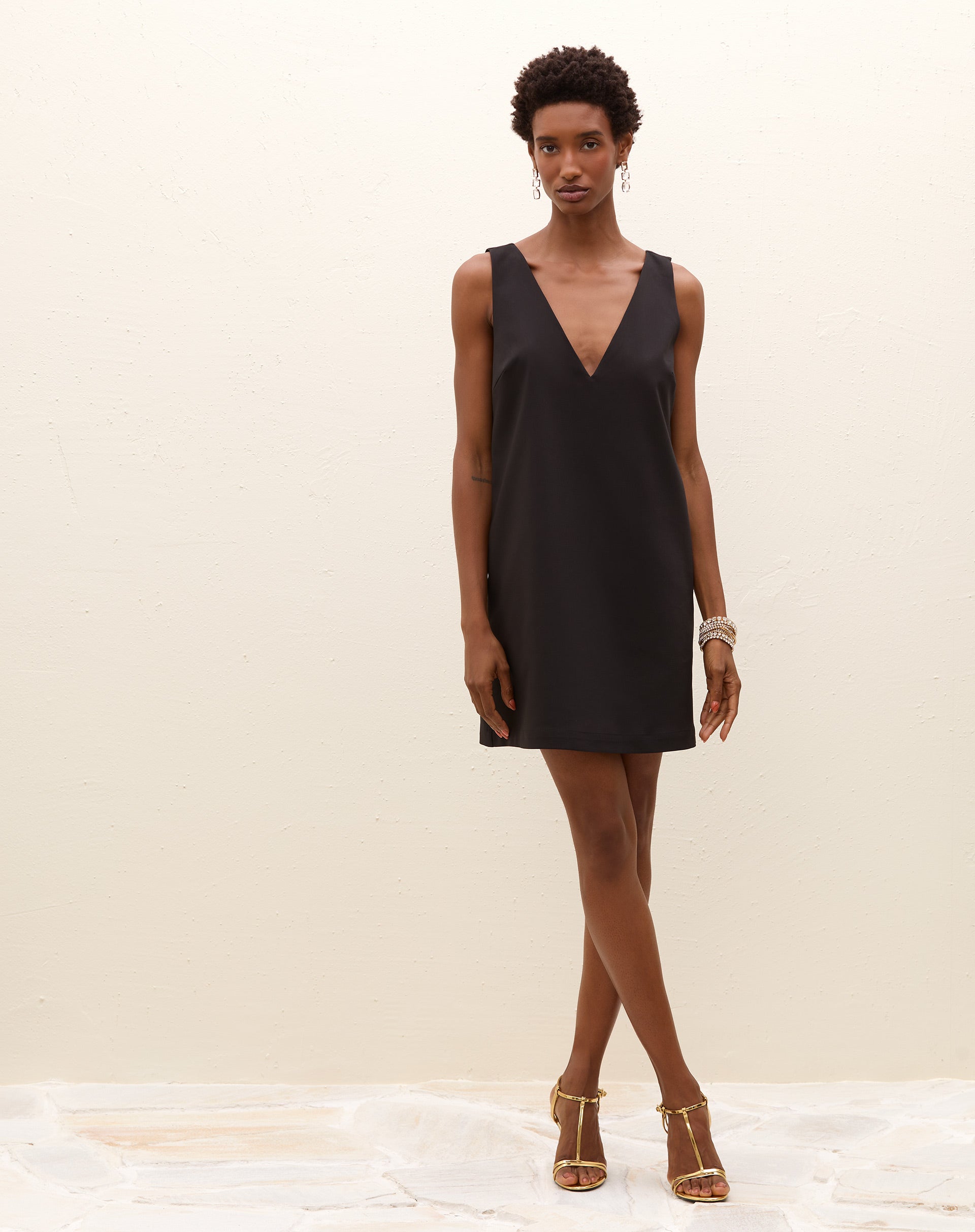 Modelo vestindo um vestido curto preto com decote V na frente, vista frontal.