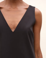 Modelo vestindo um vestido curto preto com decote V na frente, vista frontal completa.