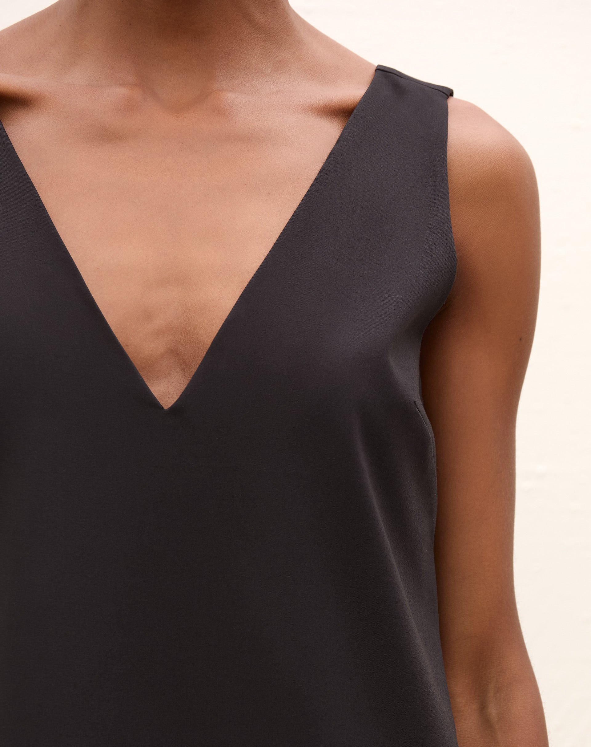 Modelo vestindo um vestido curto preto com decote V na frente, vista frontal completa.