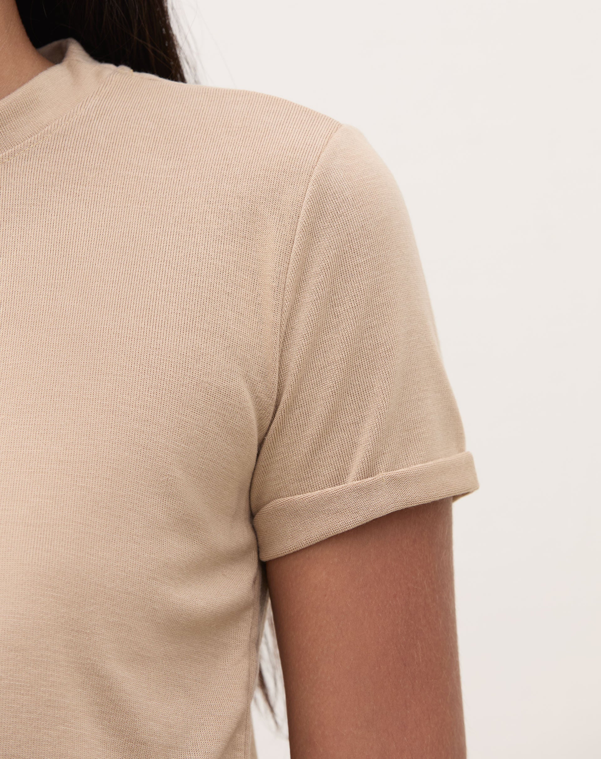 Detalhe da manga dobrada da camiseta bege.