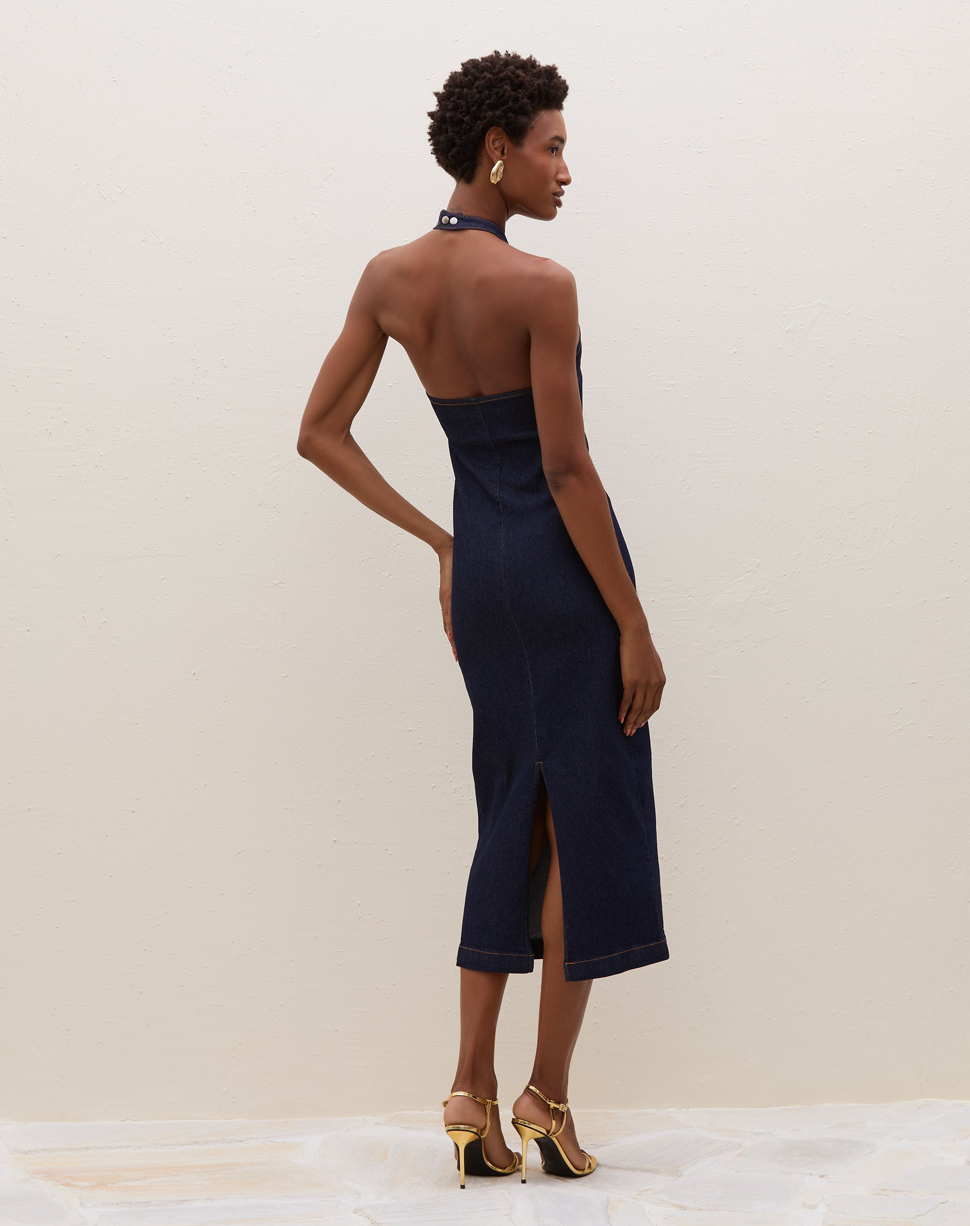 Modelo vestindo vestido midi azul escuro com decote fechado e tecido jeans, posando de costas.