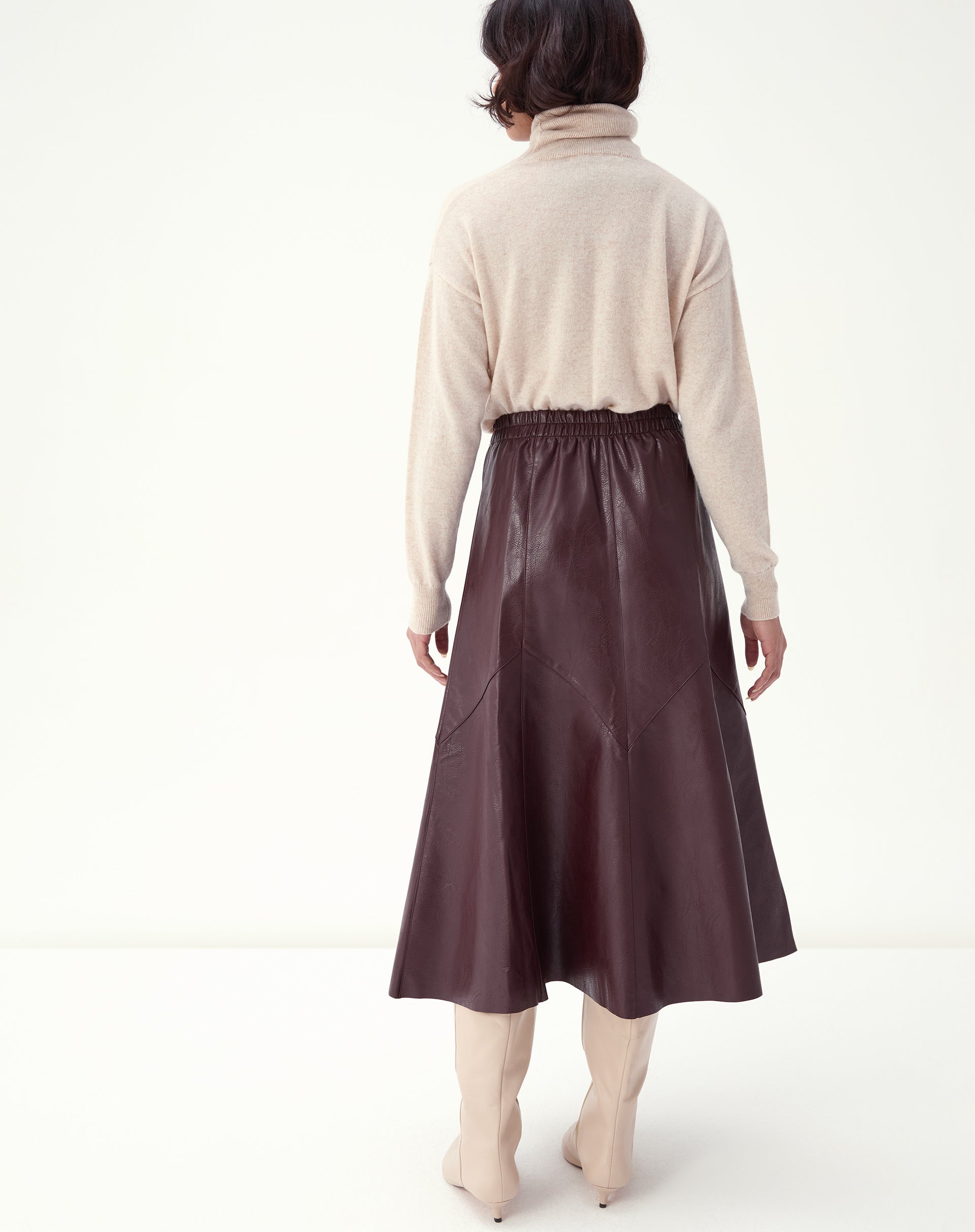 Foto frontal da saia midi burgundy em estúdio, evidenciando os recortes em painéis e o movimento do tecido com bota de cano médio