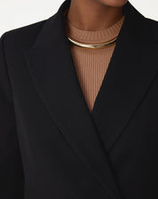 Close da lapela de ponta do blazer preto em tecido plano, mostrando o corte e acabamento de alfaiataria