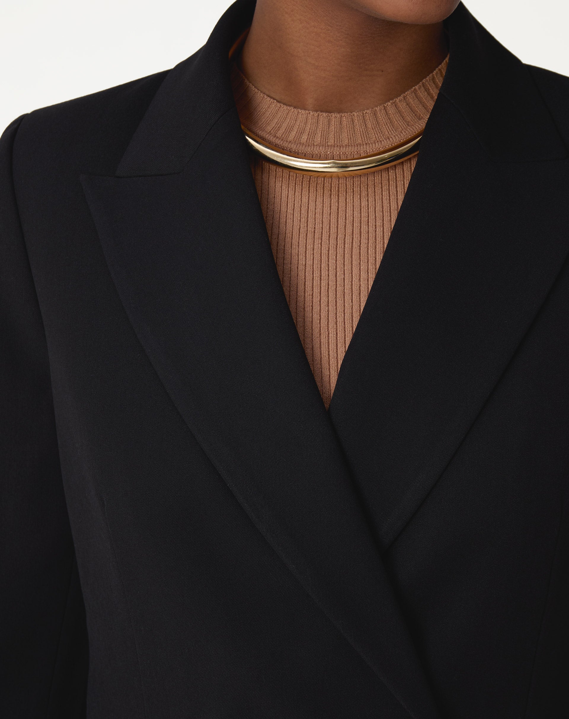 Close da lapela de ponta do blazer preto em tecido plano, mostrando o corte e acabamento de alfaiataria