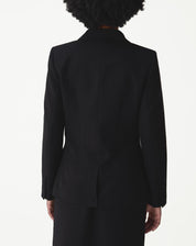 Vista traseira do blazer preto longo em modelo, com costura central e fenda única